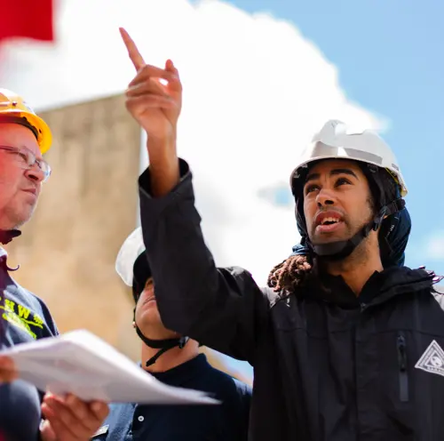 A young man in a hard hat directing a group whilst pointing.